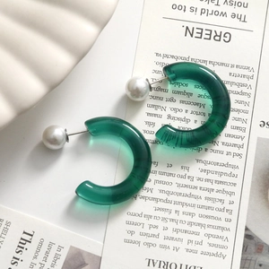 Detail of translucent dark green resin C-shape earrings with white pearl accents