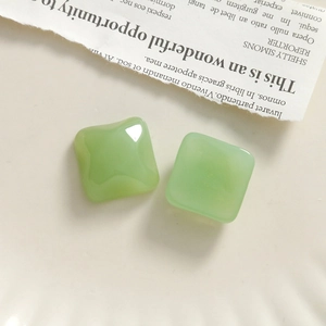 Macro detail of two light green resin square beads on a vintage newspaper background