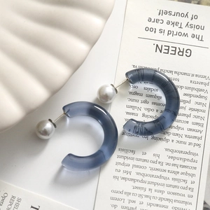 Close-up of matte blue translucent resin C-shaped hoop earrings on a shell tray