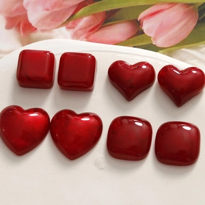 Deep red resin heart and square jewelry charms on a white tray with pink tulips