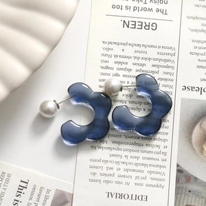 Detailed view of translucent blue floral resin earrings with white pearl accents on vintage paper
