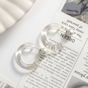 Detail of C-shaped transparent resin earrings with faux pearl on stylish background