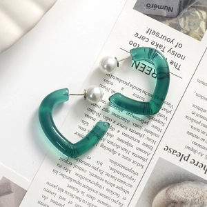 Detail of C-shaped green marble resin earrings with white pearls on a magazine