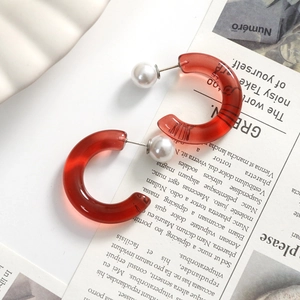 Macro detail of red resin C-shaped hoop earrings with white pearls on a stylish background