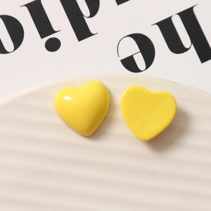 Macro shot of glossy yellow resin heart earrings on a striped ceramic tray