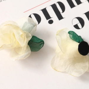 Detail of cream organza fabric flower accessory with green leaves for hair ornaments