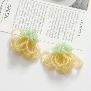 Detailed view of handmade woven flower earrings with beige beads and green crystal accents