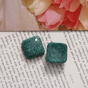 Détail de breloques carrées en résine verte avec texture craquelée sur livre ancien