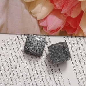 Détail de boucles d'oreilles carrées en résine avec texture fumée et craquelée sur un magazine