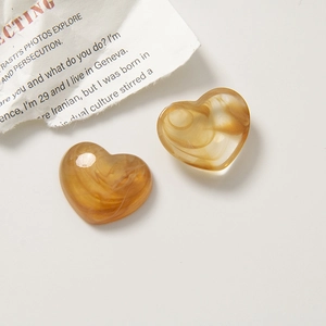 Close-up of heart-shaped amber resin charms with marble texture on white background