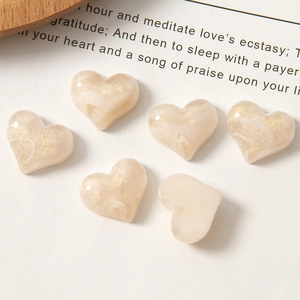 Macro detail of heart-shaped cream resin charms with gold glitter and marble texture