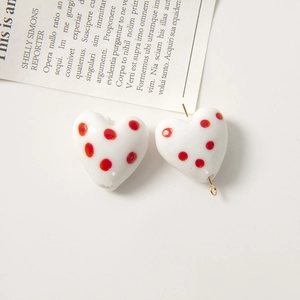 Dettaglio di perla in ceramica bianca a forma di cuore con pois rossi e gancio dorato
