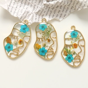 Pendente artistico in lega dorata a forma di viso con fiori secchi colorati e resina