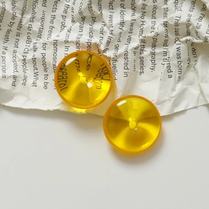 Macro detail of 20mm amber yellow translucent resin charms with center hole on paper background