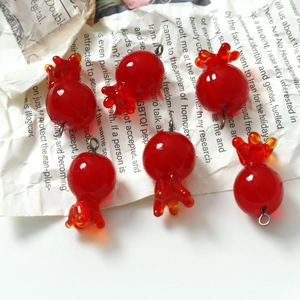 Handmade red glass pomegranate charms with metal rings for jewelry making on newspaper