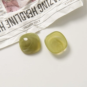 Vue à plat de perles carrées en résine vert olive avec texture marbrée sur journal