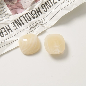 Détail de boucles d'oreilles carrées en résine marbrée crème sur journal vintage
