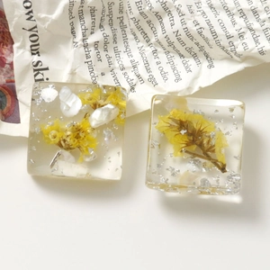 Vista macro di ciondoli quadrati in resina con fiori secchi gialli e scaglie d'argento