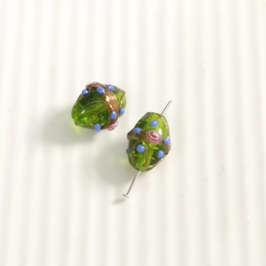 Close-up of green oval glass beads with hand-painted pink roses and blue dots
