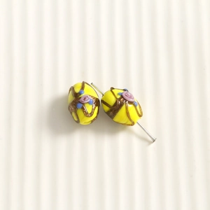 Macro shot of oval yellow glass beads with pink rose relief and gold glitter stripes