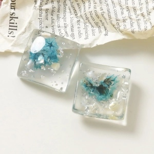 Vista macro di ciondoli quadrati in resina con fiori secchi blu e fiocchi d'argento