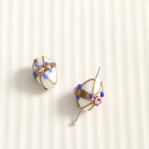 Detailed macro shot of oval white glass beads with hand-painted gold and pink floral accents