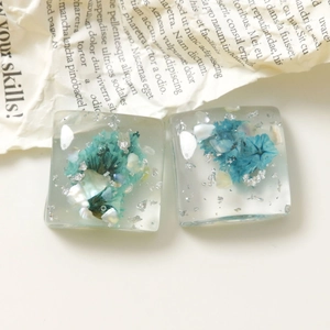 Dettaglio di ciondoli quadrati in resina con fiori secchi blu e scaglie di lamina d'argento