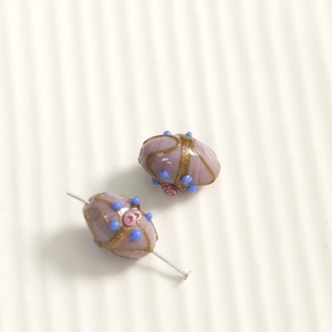 Detail of oval purple glass beads with gold glitter and pink rose floral patterns