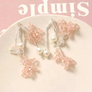 Detail of pink crystal and pearl tassel earrings on a beige plate with a soft background