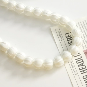 Close-up of ribbed pumpkin-shaped white glass beads arranged in a curve for DIY jewelry