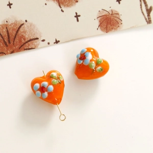 Detailed macro view of orange lampwork heart beads with floral drip oil patterns