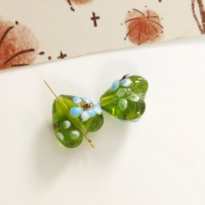 Macro detail of heart-shaped green glass beads with floral patterns and a metal pin