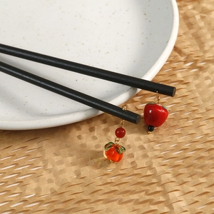 Vintage ebony hair sticks with red fruit pendants on a white ceramic plate