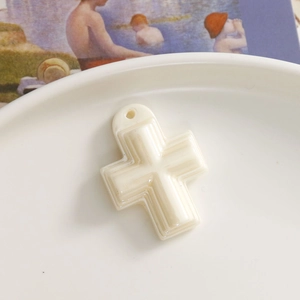 Detail eines cremeweißen Kreuzanhängers aus Harz für DIY-Schmuck auf Kunstkarte