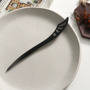 Detail of vintage ebony hair stick with hollowed teardrop design on textured tray