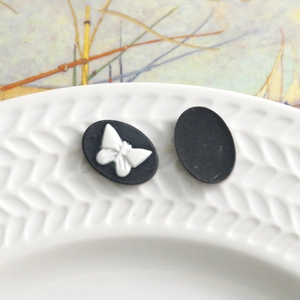 Macro detail of vintage resin oval charms with white butterfly relief on matte black base
