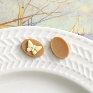 Detail of matte resin oval butterfly charms for DIY jewelry on a vintage wheat texture tray