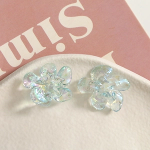 Macro shot of iridescent resin flower charms for DIY jewelry making on white textured plate