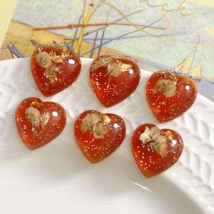 Set of 6 heart-shaped resin charms with amber flowers and gold foil on a white ceramic plate