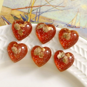 Close-up of heart-shaped resin charms with dried white flowers and gold leaf foil