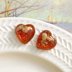 Detail of heart resin earrings with dried flowers, gold leaf, and glitter on a white tray