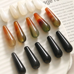 Polished teardrop agate beads in white, marbled red, and black on a ceramic tray