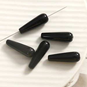 Macro view of polished black teardrop beads with central hole for DIY jewelry making