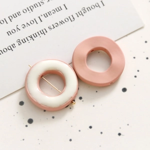 Primer plano de aretes geométricos de resina en malva mate y rosa brillante con esmalte