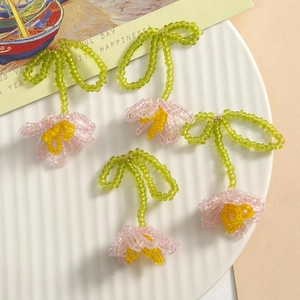 Handmade woven tulip beads earrings with pink petals and green leaves in a white ceramic dish