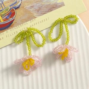 Detail of handmade beaded tulip earrings in pink and green on a white ceramic plate
