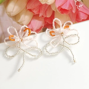 Nahaufnahme handgefertigter Blumenohrringe aus Perlen in Pink und Orange mit Quasten