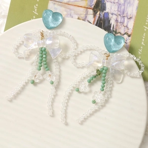 Détail de boucles d'oreilles à pompons avec cœurs bleus, nœuds blancs et perles