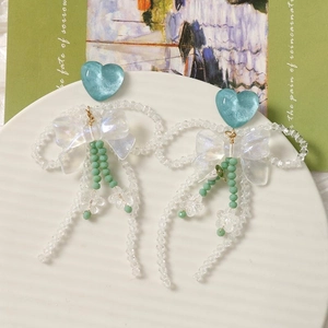 Détail de boucles d'oreilles cœur bleu avec nœuds blancs et glands en cristal sur plat