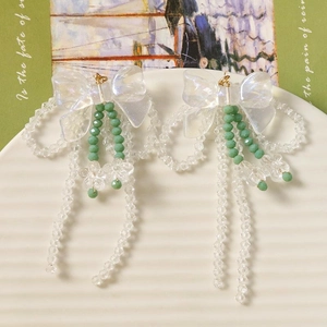 Détail macro de boucles d'oreilles nœud en acrylique avec pompons perlés et fleurs